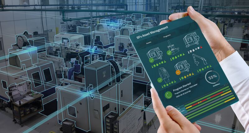 某人手里拿着的平板设备,屏幕上显示着机器的性能数据。在背景中可以看到车间的CNC机床