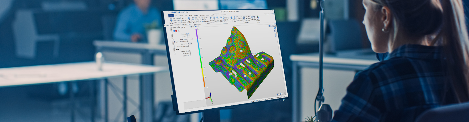 一位女士坐在办公桌前,在电脑前工作,屏幕上显示的工件是用Hexagon的再造逆向工程软件生成的